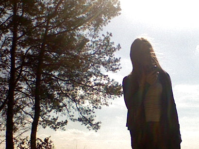Person standing in a forest with trees and sky in the background