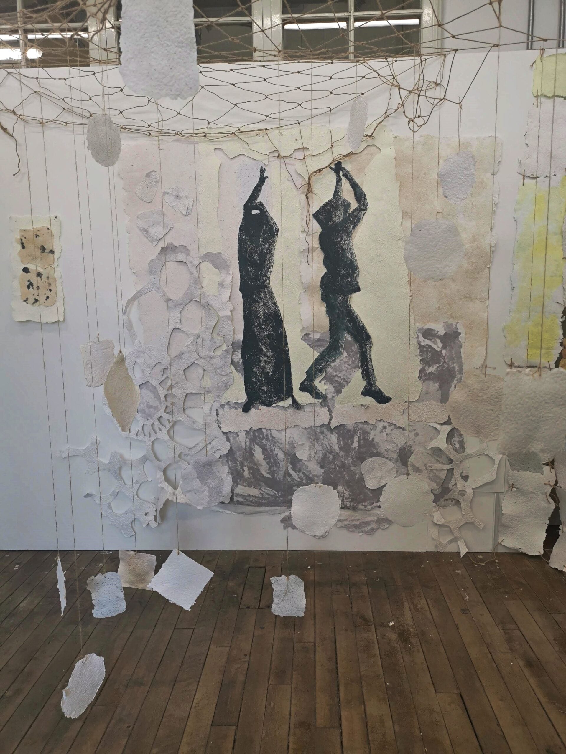 Artistic wall installation with black figures and textured paper in a room.