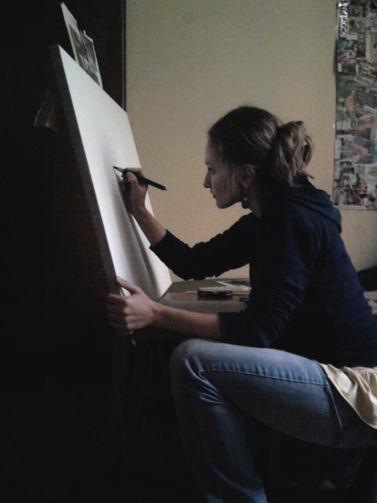Artist Paulina Pawlik painting on an easel in a room with various items on the wall.