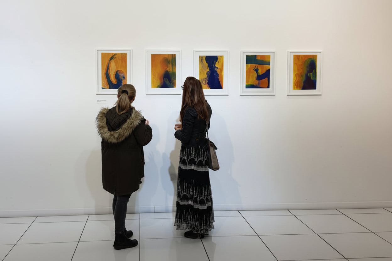 Two people looking at framed artworks on a white wall. Exhibition WOMEN Paulina Pawlik